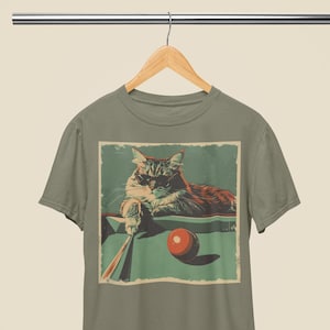 Może przedstawiać: Zielony T-shirt z ilustracją w stylu vintage kota w okularach przeciwsłonecznych grającego w bilard. Kot siedzi na zielonym stole bilardowym z czerwoną kulą bilardową przed nim.