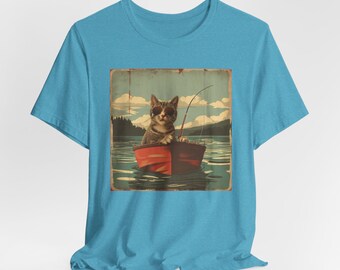May include: A bright blue short-sleeve t-shirt featuring a square graphic print of a tabby cat wearing sunglasses, sitting in a small red rowboat on a lake while holding a fishing rod, set against a backdrop of distant mountains and a cloudy sky.