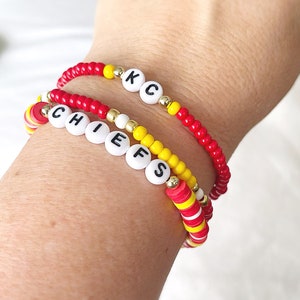 May include: Three beaded bracelets in red, yellow, and white. One bracelet spells "CHIEFS" with white letter beads. Another spells "KC". The bracelets are stacked on a wrist, showcasing the team colors.