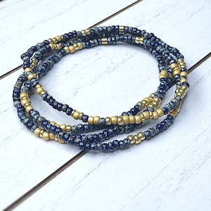 May include: A multi-strand beaded necklace featuring blue and gold beads. The necklace is crafted from small, round beads arranged in a repeating pattern. The beads are a dark blue shade with a speckled design, and the gold beads are a bright, shiny gold.