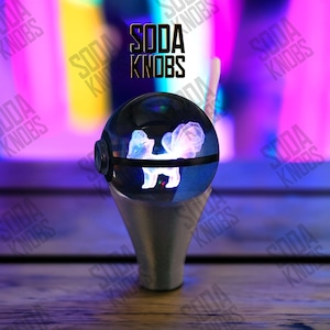 Pode incluir: Um botão de refrigerante decorativo com um topo esférico transparente com um design de água-viva branco e rosa brilhante. O botão tem uma base prateada e o texto "SODA KNOBS" é visível no fundo.