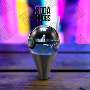 May include: A clear, spherical soda knob with a black and white design, featuring a white creature inside. The knob sits on a silver-coloured base. The text "SODA KNOBS" is displayed above the knob.