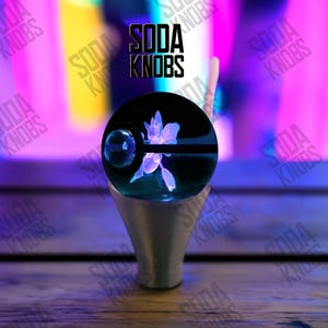 Peut inclure: Un bouton de soda personnalisé avec un globe noir orné d'un motif floral bleu brillant. Le bouton est monté sur une base argentée. Le texte "SODA KNOBS" est affiché au-dessus du globe.