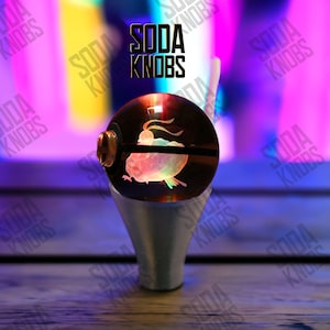 Könnte beinhalten: Ein dekorativer Soda-Knauf mit einer transparenten, kugelförmigen Oberseite mit einem farbenfrohen Fischdesign. Der Knauf hat einen silberfarbenen Sockel und der Text "SODA KNOBS" ist im Hintergrund sichtbar.