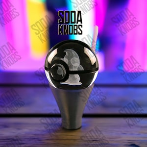 Könnte beinhalten: Ein schwarzer und klarer Soda-Knauf mit einem weißen geätzten Design im Inneren. Der Knauf hat einen silbernen Sockel und der Text "SODA KNOBS" befindet sich über dem Knauf. Der Hintergrund ist eine verschwommene Mischung aus Lila, Gelb und Rosa.