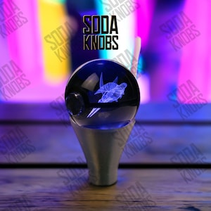 Könnte beinhalten: Ein blauer Soda-Knauf aus Glas mit einem 3D-Schildkröten-Design. Der Knauf steht auf einem silberfarbenen Sockel. Der Text "SODA KNOBS" ist in Schwarz über dem Knauf zu sehen.