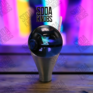 May include: A black and blue soda knob with a glowing creature design inside. The knob is mounted on a silver base. The text "SODA KNOBS" is displayed in black above the knob.