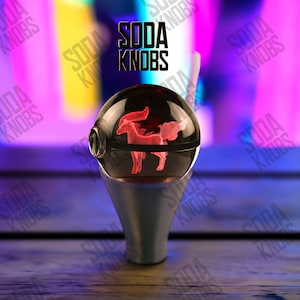 Peut inclure: Un bouton de soda sphérique transparent avec une silhouette de cheval rouge et lumineuse à l'intérieur. Le bouton repose sur une base argentée. Le texte "SODA KNOBS" est affiché au-dessus du bouton en noir.