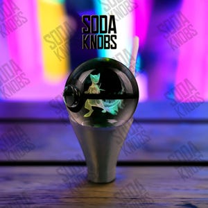 Könnte beinhalten: Ein individueller Soda-Knauf mit einem transparenten, kugelförmigen Design und einem Pokémon-Charakter im Inneren. Der Knauf ist auf einem silberfarbenen Sockel montiert. Der Text "SODA KNOBS" wird über dem Knauf angezeigt.