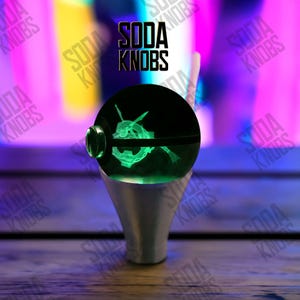 Op de afbeelding: Een aangepaste sodaknop met een gloeiend groen ontwerp in een heldere bol. De knop is gemonteerd op een zilverkleurige basis. De tekst "SODA KNOBS" staat boven de knop.