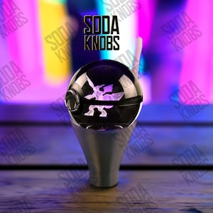Peut inclure: Un bouton de soda noir et transparent avec un motif graphique violet. Le bouton a une base argentée et le texte "SODA KNOBS" est visible en arrière-plan.