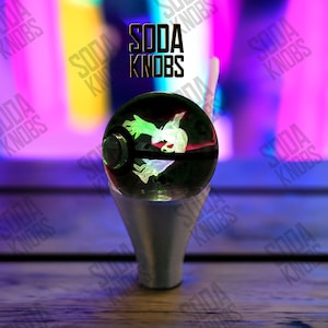 Könnte beinhalten: Ein schwarzer und grüner Schaltknauf mit einer leuchtenden weiß-grünen Grafik. Der Schaltknauf ist auf einem silbernen Sockel montiert. Der Text "SODA KNOBS" wird über dem Schaltknauf angezeigt.