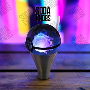 May include: A custom gear stick knob with a clear, spherical top displaying a glowing blue and purple design. The knob has a silver base and a black band around the sphere. The text "SODA KNOBS" is above the knob.