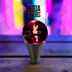Könnte beinhalten: Ein individueller Soda-Knauf mit rotem und schwarzem Design, der eine Charakterillustration zeigt. Der Knauf ist auf einem silbernen Sockel montiert. Der Text "SODA KNOBS" wird über dem Knauf angezeigt.