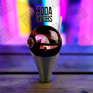 Könnte beinhalten: Ein einzigartiger, kugelförmiger Soda-Knauf mit einer dunklen, durchscheinenden Kugel, die ein beleuchtetes Innendesign zeigt. Der Knauf ist auf einem silberfarbenen Sockel montiert. Der Text "SODA KNOBS" ist über dem Knauf zu sehen.
