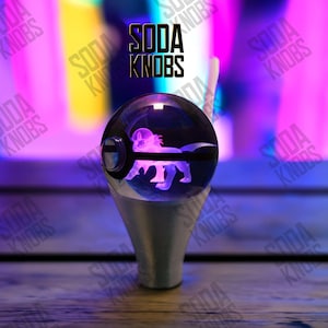 Könnte beinhalten: Ein klarer, kugelförmiger Schalthebelknauf mit einem leuchtenden lila Kreaturen-Design im Inneren. Der Knauf sitzt auf einem silbernen Sockel. Der Text "SODA KNOBS" wird in Schwarz angezeigt.