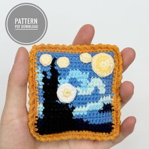Puede incluir: Un cuadrado tejido a crochet con una escena de noche estrellada azul, blanca y amarilla. El cuadrado está enmarcado con un borde naranja tejido a crochet. El texto "PATTERN PDF DOWNLOAD" está en un círculo sobre el cuadrado.