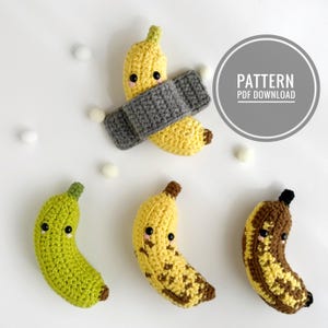 May include: Four crocheted banana plushies with black bead eyes and pink cheeks. One yellow banana is taped with a gray crocheted strip. The others are solid green, yellow with brown spots, and brown with yellow spots. Text reads PATTERN PDF DOWNLOAD.