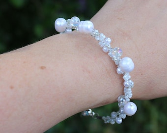 May include: A delicate bracelet featuring white pearls and clear beads. The bracelet is strung together with a silver-colored wire, creating a shimmering effect. The pearls are of varying sizes, adding visual interest to the jewelry.
