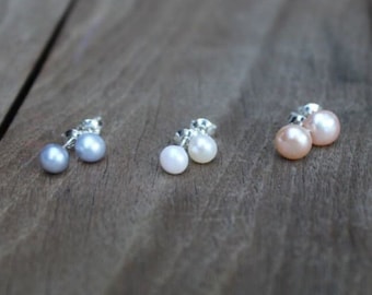 May include: Three pairs of pearl stud earrings in silver settings. The earrings are in shades of gray, white, and pink.