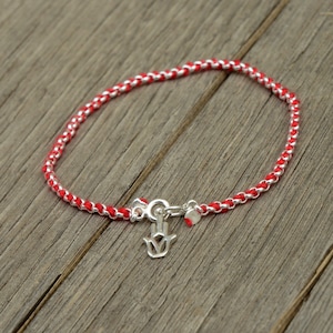 May include: A red and silver bracelet with a hamsa charm. The bracelet is made of a braided red cord and a silver chain.