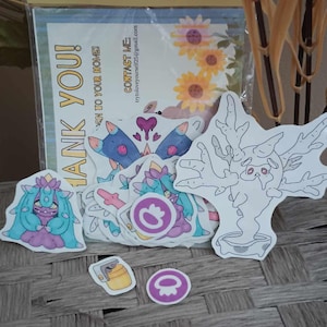 May include: A set of colorful stickers featuring cartoon characters. The stickers are on a white background and include a purple and blue butterfly, a pink and blue creature with a flower on its head, and a white tree-like creature. The stickers are packaged in a clear plastic bag with a yellow label that says "Swedish Scribble Poke Pack".
