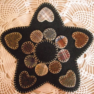 May include: A black felt star-shaped trivet with a variety of patterned fabric hearts and circles sewn on. The trivet is surrounded by a white crocheted doily.