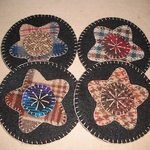 May include: Four black felt coasters with a star design. Each coaster features a different patterned fabric in shades of brown, red, blue, and white.