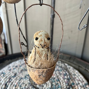 May include: A small, brown, and white bird with black eyes sits in a brown, textured egg-shaped nest. The nest is hanging from a wire loop.