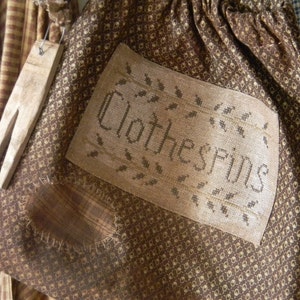 May include: A brown fabric bag with a white embroidered design that says "Clothes Pins". The bag has a brown and white checkered pattern.