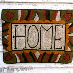 May include: A beige and brown rug with the word "HOME" in black lettering. The rug has a decorative border with hearts and geometric patterns.