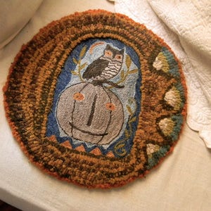 May include: A brown, round rug with a woven design featuring a pumpkin, an owl, and floral motifs. The rug has a textured surface and is made of wool.