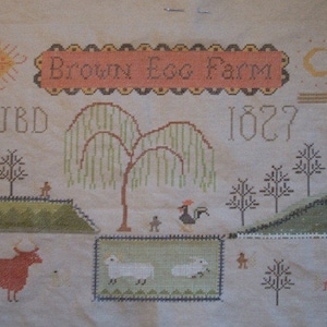 May include: A cross-stitch sampler featuring a farmhouse scene with a weeping willow tree, a red barn, a white house, a key, a sun, a moon, a rooster, sheep, and a cow. The sampler is titled "Brown Egg Farm" and dated "1827".