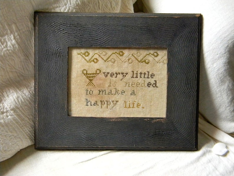 May include: A black wooden frame with a white background and the text "very little is needed to make a happy life." The text is in a decorative font and is surrounded by a border of small, stylized flowers.