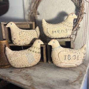 May include: Four handmade fabric chickens with embroidered details. The chickens are beige with brown stitching and have different embroidered text on their bodies. The text reads "Hens" and "1831".