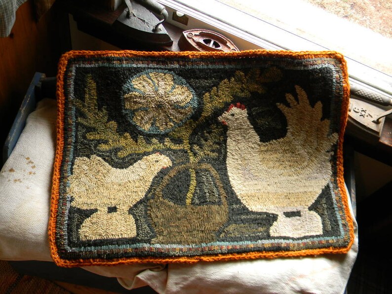 May include: A hand-stitched rug with an orange border features two white chickens with brown eyes and a floral design in the background.