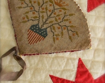 May include: A hand-stitched fabric ornament featuring a stylized tree with red, white, and blue accents. The ornament is attached to a white fabric background with red stars.