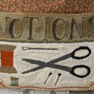 May include: A white rug with the word "NOTIONS" in brown lettering. The rug depicts a spool of thread, scissors, needles, and a thimble.