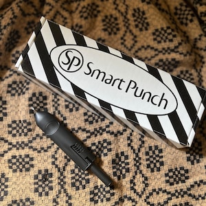May include: A black Smart Punch tool with a white and black striped box. The box has the text "SP Smart Punch" on it.