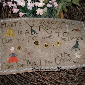 May include: A cross-stitch sampler with a beige background and brown, black, and white embroidery. The sampler features the text "Plant Ye Seeds All In A Row One To Tot One To Crow The One For Me 1 For Crow" and images of a beehive, a bird, a sunflower, and a crow.