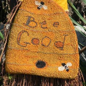 May include: A yellow and orange doormat with the words "Bee Good" embroidered in brown. The doormat is shaped like a honeycomb and has two small bees embroidered on it.