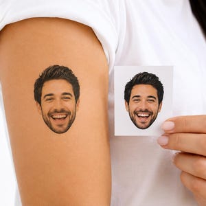 Könnte beinhalten: Ein temporäres Tattoo mit einem realistischen Farbporträt einer lächelnden Person mit dunklem Haar und Bart, das auf die Haut aufgetragen wurde, neben einer quadratischen weißen Papierkarte, die das identische Porträt derselben Person zeigt.