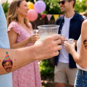 May include: A temporary tattoo featuring a colorful illustration of a person's face with a mustache, glasses, and a striped party hat. The design includes small confetti accents in red, yellow, and green, applied to the skin of two different individuals.