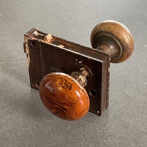 May include: Antique door hardware with a brass knob and a brown, marbled ceramic knob. The hardware is attached to a metal plate.