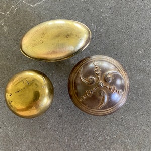 May include: Three vintage brass trinket boxes. One box is oval shaped with a smooth surface. The second box is round with a floral design. The third box is round with a smooth surface.