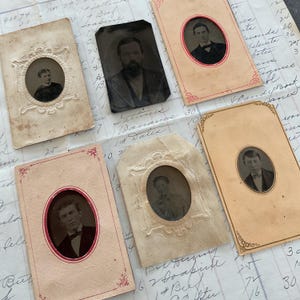 May include: Collection of vintage portrait photographs in ornate frames. The photos are in black and white and feature people in formal attire. The frames are made of paper and have a decorative design.