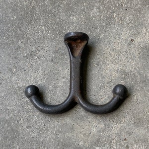 May include: A black cast iron double hook with rounded ends. The hook is designed to be mounted on a wall or other surface.