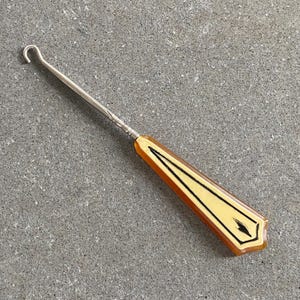 May include: A silver shoe horn with a yellow and black handle. The handle has a geometric design.