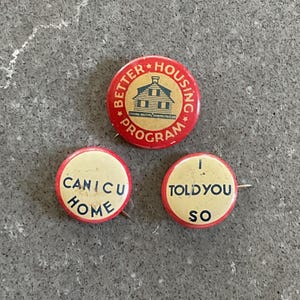 May include: Three circular pinback buttons with red borders. The top button is red with a tan center, featuring a house graphic and the text BETTER HOUSING PROGRAM. The bottom left button says CAN I C U HOME, and the bottom right says I TOLD YOU SO.