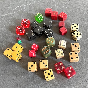 May include: A collection of assorted six-sided dice in various colours including red, black, green, yellow, and cream. The dice feature different styles of pips, ranging from standard dots to circular outlines, and include both opaque and translucent finishes.